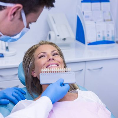 doctor-holding-tooth-whitening-equipment-by-smiling-patient (1) (1)